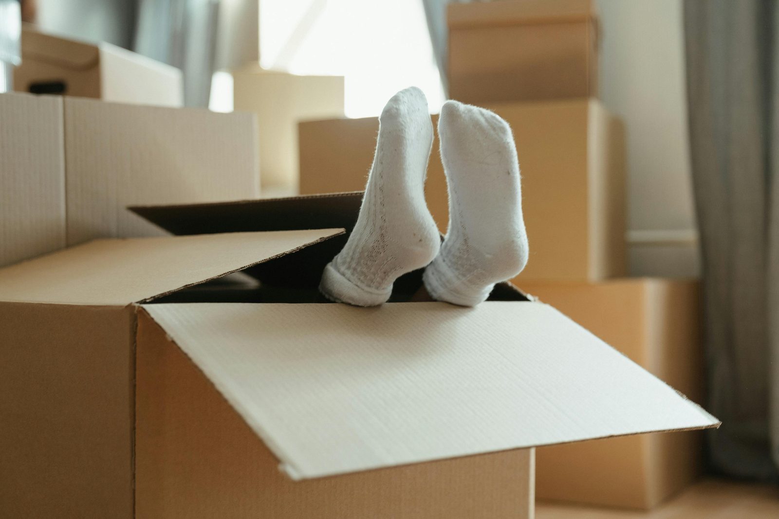 Feet in white socks sticking out of a moving box surrounded by packed cardboard boxes